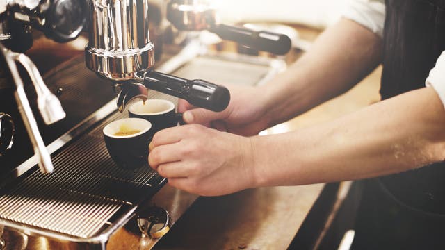 Zwei gefüllte Espressotassen unter der Düse einer Kaffeemaschine.