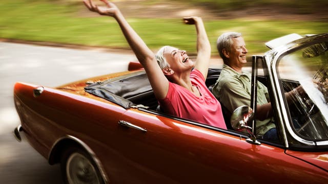 Ein glückliches älteres Paar fährt mit dem Cabrio in den Sonnenuntergang