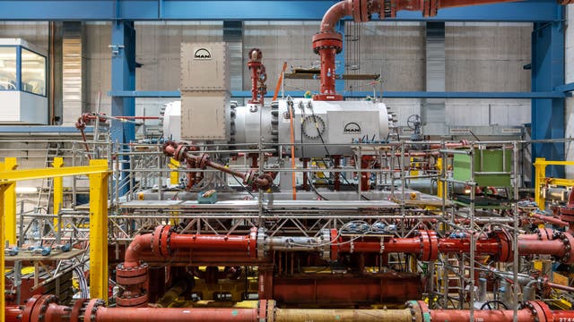 Großwärmepumpe mit komplexem Rohrleitungssystem und Maschinen in einer Halle. Im Zentrum befindet sich ein großer, zylindrischer Behälter mit dem Logo der Firma "MAN".