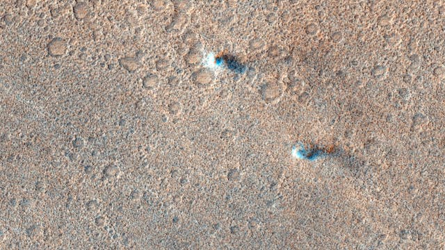 Eine hochauflösende Aufnahme der Marsoberfläche, die eine Vielzahl kleiner, kreisförmiger Krater zeigt. Die Oberfläche erscheint sandig und weist eine ungleichmäßige Textur auf. Einige Krater sind von dunkleren Schatten umgeben, was auf eine unterschiedliche Tiefe oder Materialzusammensetzung hinweisen könnte. Die Farbgebung ist überwiegend in erdigen Tönen gehalten, mit vereinzelten helleren und dunkleren Bereichen, die möglicherweise auf geologische Aktivitäten oder Erosion hindeuten.