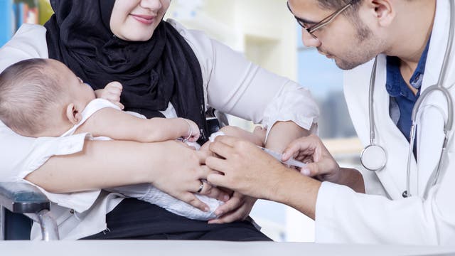 Ein junger Arzt impft ein Kleinkind, das von seiner Mutter gehalten wird