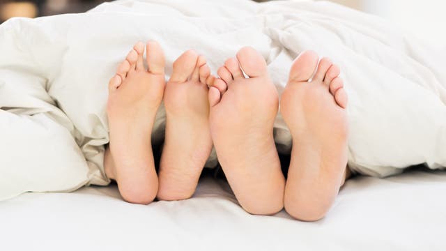 Zwei Paar Füße, die unter einer zu kurzen Bettdecke herausgucken