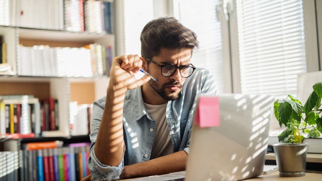 Ein junger Mann sitzt am Schreibtisch vorm Rechner, in die Arbeit vertieft