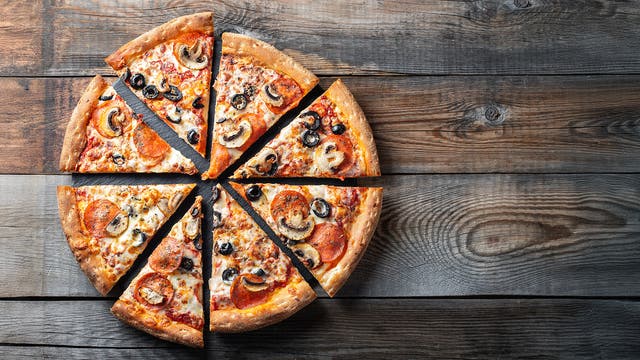 Eine Pizza in acht gleichmäßige Stücke geschnitten, mit knuspriger Kruste, belegt mit Salami, Pilzen, schwarzen Oliven und geschmolzenem Käse, liegt auf einem rustikalen Holztisch.