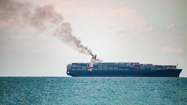 Ein Containerschiff fährt auf dem Meer, aus dem Schornstein steigt schwarzer Rauch auf.