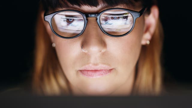 Eine Person mit Brille schaut auf einen Computerbildschirm. Der Bildschirm spiegelt sich in den Brillengläsern wider. Die Szene ist in einem dunklen Raum aufgenommen, was auf konzentriertes Arbeiten oder Surfen im Internet hindeutet.