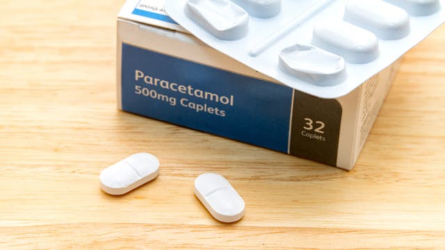 Eine Packung Paracetamol-Tabletten mit der Aufschrift „Paracetamol 500mg Caplets“ und „32 Caplets“ auf der Verpackung. Zwei weiße Tabletten liegen auf einer Holzoberfläche vor der geöffneten Blisterpackung.