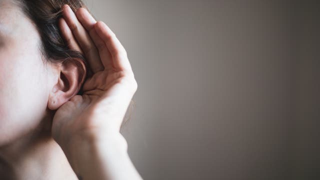 Eine Person hält ihre Hand hinter ihr Ohr, als ob sie versucht, besser zu hören. Der Hintergrund ist unscharf und neutral, was den Fokus auf die Geste lenkt. Diese Darstellung könnte auf das Thema Zuhören oder Aufmerksamkeit hinweisen.