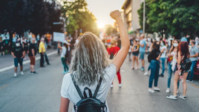 Eine Frau läuft einer Demonstration entgegen und streckt die Faust in die Höhe