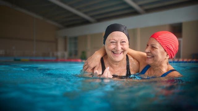 Zwei Seniorinnen umarmen sich im Wasser im Hallenbad