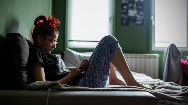 Jugendliche sitzt auf dem Bett und schaut auf ihr Smartphone 