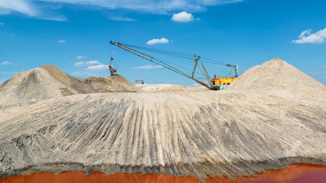 Eine große industrielle Baggermaschine fördert Sand auf einem Hügel in einem Tagebau. 