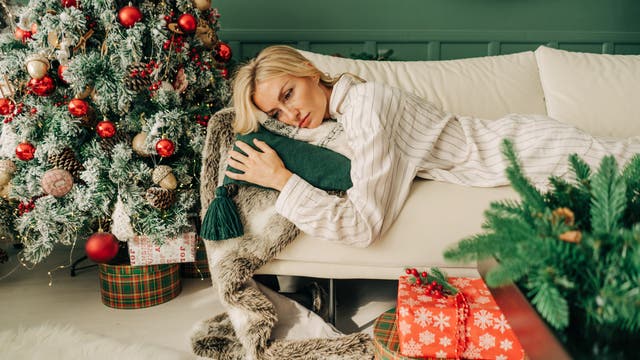 Eine müde aussehende Frau liegt auf einem Sofa neben einem geschmückten Weihnachtsbaum.