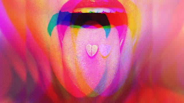 Ein Mund mit leuchtend roten Lippen ist weit geöffnet, die Zunge herausgestreckt. Auf der Zunge liegt eine herzförmige Tablette. Das Bild ist in lebendigen, psychedelischen Farben gehalten, die einen Regenbogeneffekt erzeugen. Es gibt keinen Text im Bild und keine verlinkte URL.