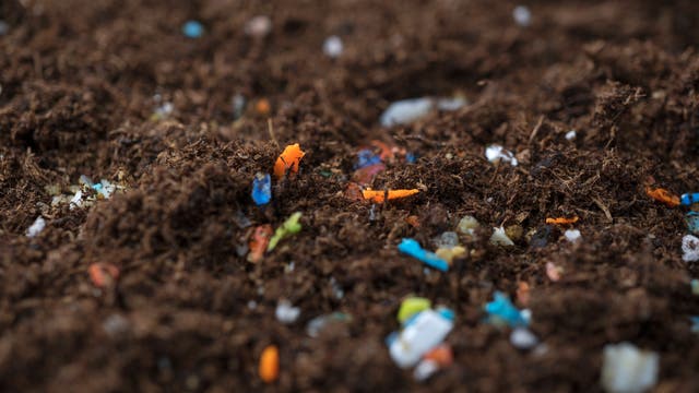 Erde mit verstreuten Mikroplastikstücken in verschiedenen Farben wie Blau, Orange und Weiß. Die Aufnahme zeigt die Umweltverschmutzung durch Plastikabfälle im Boden.