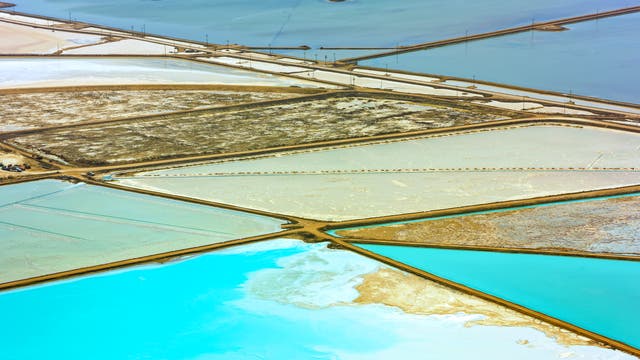 eine Luftaufnahme zeigt eine Anordnung von Verdunstungsbecken einer Lithium-Mine von oben; vorn leuchten zwei Becken in türkis-blau, in den dahinter liegenden ist eher eine bräunliche bis schlammige Brühe zu sehen. Rechts scheinen die Becken an ein offenes Gewässer zu grenzen