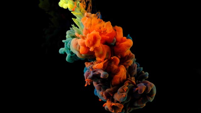 Eine abstrakte Kunstabbildung zeigt leuchtende Farbwolken in Orange, Blau und Grün, die sich in einer fließenden Bewegung vor einem schwarzen Hintergrund vermischen. Die Farben scheinen sich dynamisch zu entfalten und erzeugen einen lebendigen Kontrast zur Dunkelheit des Hintergrunds. Die Komposition vermittelt ein Gefühl von Bewegung und Kreativität.