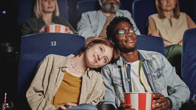 Pärchen sitzt glücklich im Kino, sie hat ihren Kopf auf seine Schulter gelegt