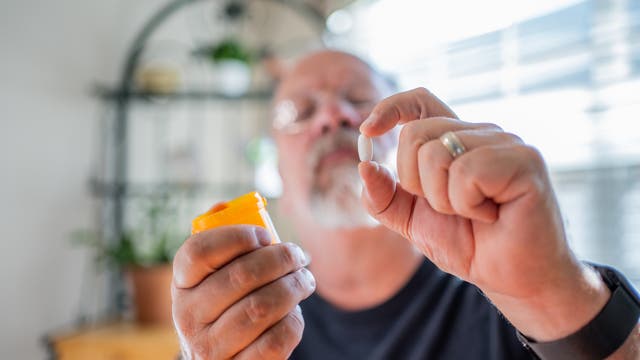 Älterer Mann begutachtet skeptisch eine Pille in seiner linken Hand und hält in der rechten eine Pillendose.