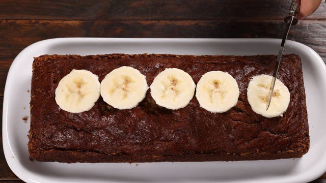 Aufsicht auf einen Kastenkuchen, der mit Bananenscheiben garniert ist und gerade angeschnitten werden soll