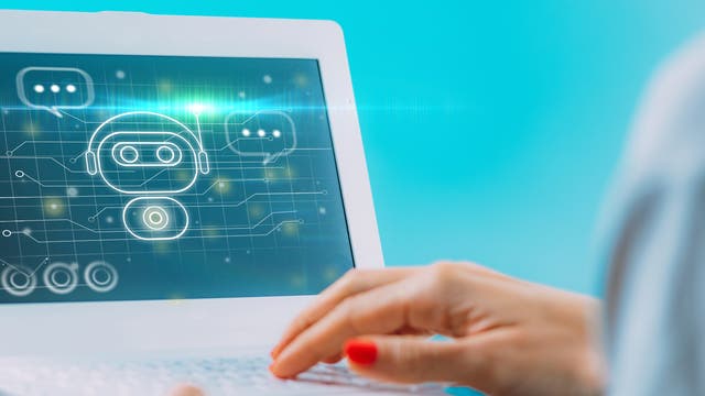 Eine Person tippt auf einem Laptop mit einem blauen Bildschirm, auf dem ein digitales Symbol eines Chatbots mit Sprechblasen und Schaltkreisen angezeigt wird. Das Bild vermittelt das Thema künstliche Intelligenz und digitale Kommunikation.