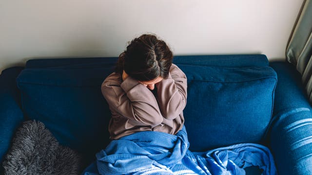 Junge Frau sitzt auf einem blauen Sofa und hält sich den Nacken mit beiden Händen