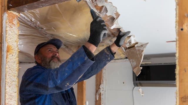 Ein Arbeiter entfernt ohne Mundschutz die Deckenverkleidung in einem Haus