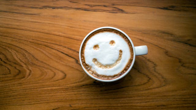 Eine Tasse Cappuccino auf einem Holztisch, mit einem Smiley-Gesicht aus Milchschaum auf der Oberfläche des Kaffees.