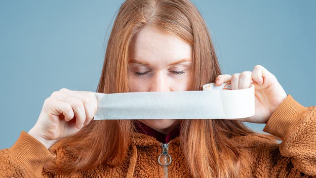 Rothaarige junge Frau klebt sich den Mund mit Panzertape zu.