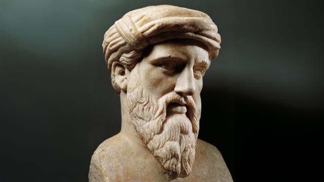 Eine Marmorbüste eines antiken Philosophen mit einem detailliert geschnitzten Bart und einem turbanähnlichen Kopfschmuck. Die Skulptur zeigt einen ernsten Ausdruck und ist vor einem neutralen Hintergrund platziert.