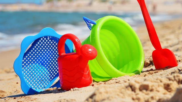 Sieb, Gießkanne, Eimer und Schaufel aus grellbuntem Plastik stehen im Sand an einem Strand