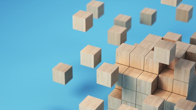 Eine 3D-Darstellung von hölzernen Würfeln, die in einem Raster angeordnet sind. Einige Würfel scheinen sich vom Hauptblock zu lösen und schweben in der Luft. Der Hintergrund ist einfarbig blau, was den Fokus auf die geometrische Anordnung der Würfel lenkt.