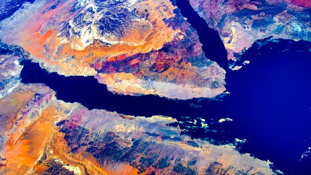 Satellitenbild einer geografischen Karte, die das Rote Meer und die umliegenden Regionen zeigt. Die Karte hebt die kontrastreichen Farben der Wüstenlandschaften und die tiefblaue Farbe des Meeres hervor. Die Küstenlinien sind deutlich sichtbar, und die topografischen Merkmale der Halbinsel und der angrenzenden Landmassen sind detailliert dargestellt. Das Bild vermittelt einen Eindruck von der geologischen Vielfalt und der geografischen Lage der Region.