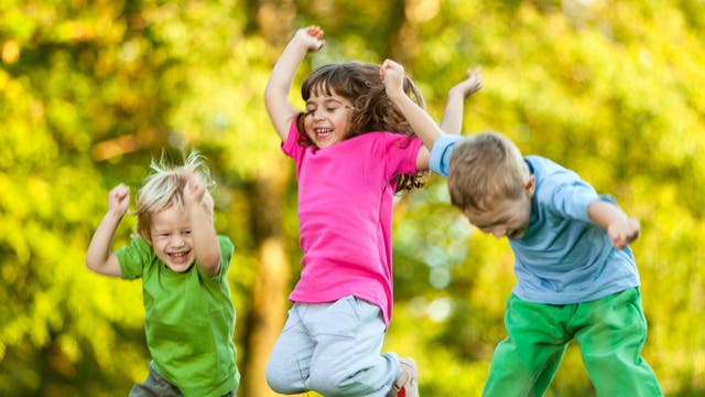 Drei kleine Kinder springen lachend unter freiem Himmel umher.