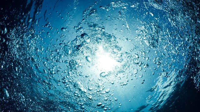Blasen steigen aus tiefblauem Wasser an die Oberfläche