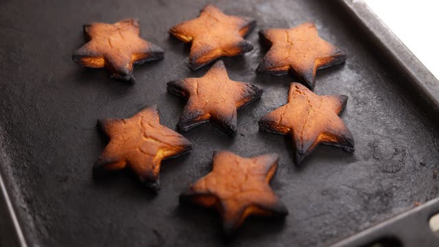 Foto von an den Ecken verbrannten sternförmigen Weihnachtsplätzchen, die auf einem Blech aus dem Backofen geholt werden