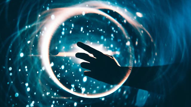 Eine Hand streckt sich in Richtung eines leuchtenden, kreisförmigen Lichts in einem dunklen, blauen Hintergrund. Um den Kreis herum sind helle, funkelnde Punkte verteilt, die an Sterne erinnern. Die Szene vermittelt ein Gefühl von Technologie und Magie.