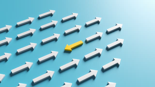 Eine Gruppe weißer Pfeile zeigt nach rechts auf einem blauen Hintergrund. Ein gelber Pfeil in der Mitte zeigt nach links, was symbolisch für Andersdenken oder Individualität steht.