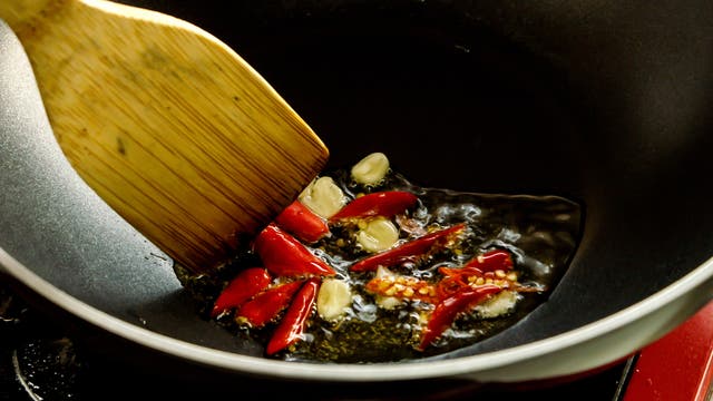 Chili und Knoblauch werden in einer Pfanne mit Öl angebraten.