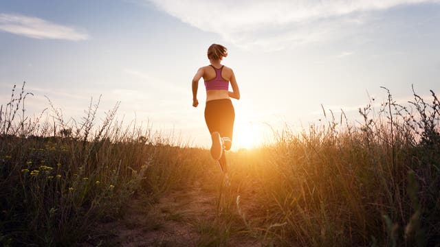 Eine Frau in Sportkleidung joggt in die untergehende Sonne.