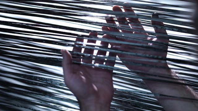 Zwei Hände berühren mehrere parallele, glänzende Fäden oder Drähte, die in horizontalen Linien gespannt sind. Das Licht reflektiert auf den Drähten und erzeugt ein Spiel aus Licht und Schatten. Die Szene vermittelt ein Gefühl von Interaktion und Erkundung.