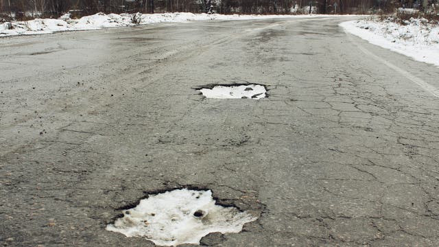 Im rissigen Asphalt einer Straße im Winter klaffen große, mit verfestigtem Schnee gefüllte Schlaglöcher