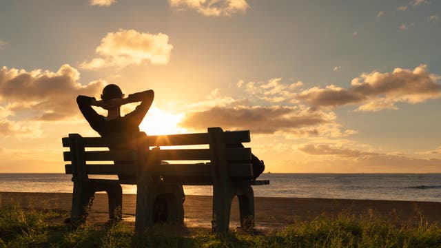 Eine Frau sitzt entspannt auf einer Bank und schaut in den Sonnenuntergang