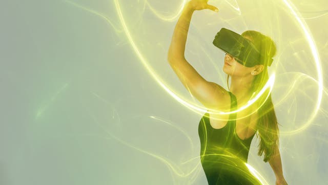 Eine Frau trägt ein Virtual-Reality-Headset und hebt tänzerisch die Hand, wobei sie virtuelle Lichtkreise in Gelb hinterlässt, die sie umgeben. Sie trägt ein schwarzes ärmelloses Oberteil. Die Szene ist in grünlich gelbes Licht getaucht, was eine futuristische Atmosphäre schafft.