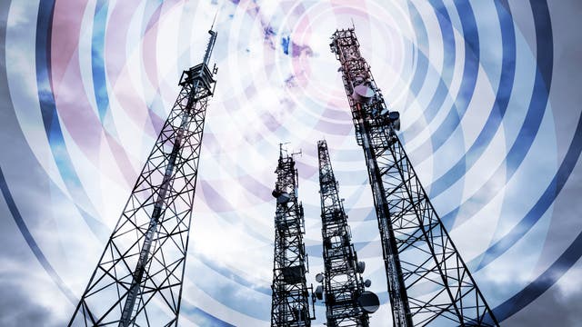 Mehrere hohe Sendemasten ragen in den bewölkten Himmel, umgeben von konzentrischen Kreisen, die Funkwellen darstellen. Die Masten sind mit verschiedenen Antennen und Satellitenschüsseln ausgestattet.
