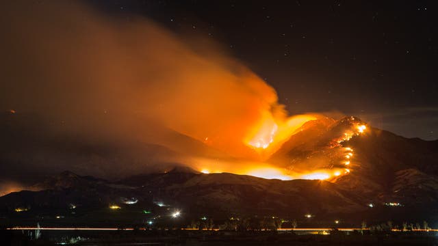 Waldbrand in den Bergen über einer Küste bei Nacht.