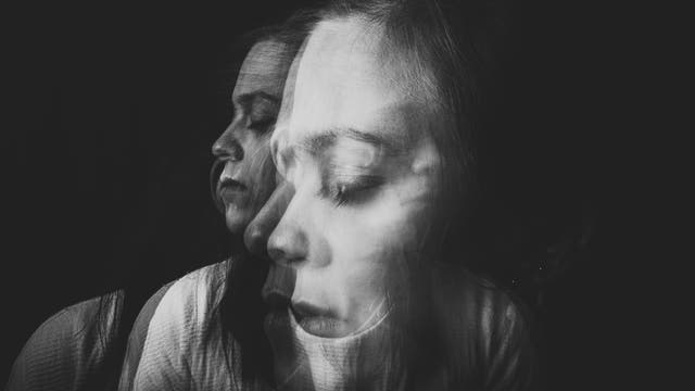 Eine künstlerische Schwarz-Weiß-Doppelbelichtung eines nachdenklichen Gesichts, das in zwei Richtungen blickt. Die Person hat geschlossene Augen, was einen meditativen oder träumerischen Zustand suggeriert. Der Hintergrund ist dunkel, wodurch das Gesicht im Vordergrund hervorgehoben wird. Es gibt keinen Text oder eine URL im Bild.