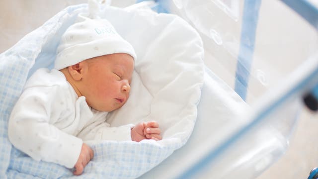 Ein kleines Baby mit Mützchen auf dem Kopf schläft im Bettchen auf der Säuglingsstation.