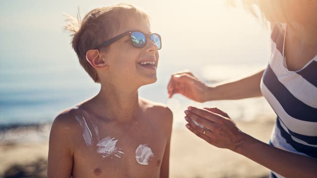 Eine Mutter schmiert ihren Sohn an einem sonnigen Tag am Strand mit Sonnencreme ein.