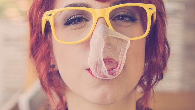 Eine rothaarige junge Frau mit gelber Brille hat eine geplatzte Kuagummiblase im Gesicht.